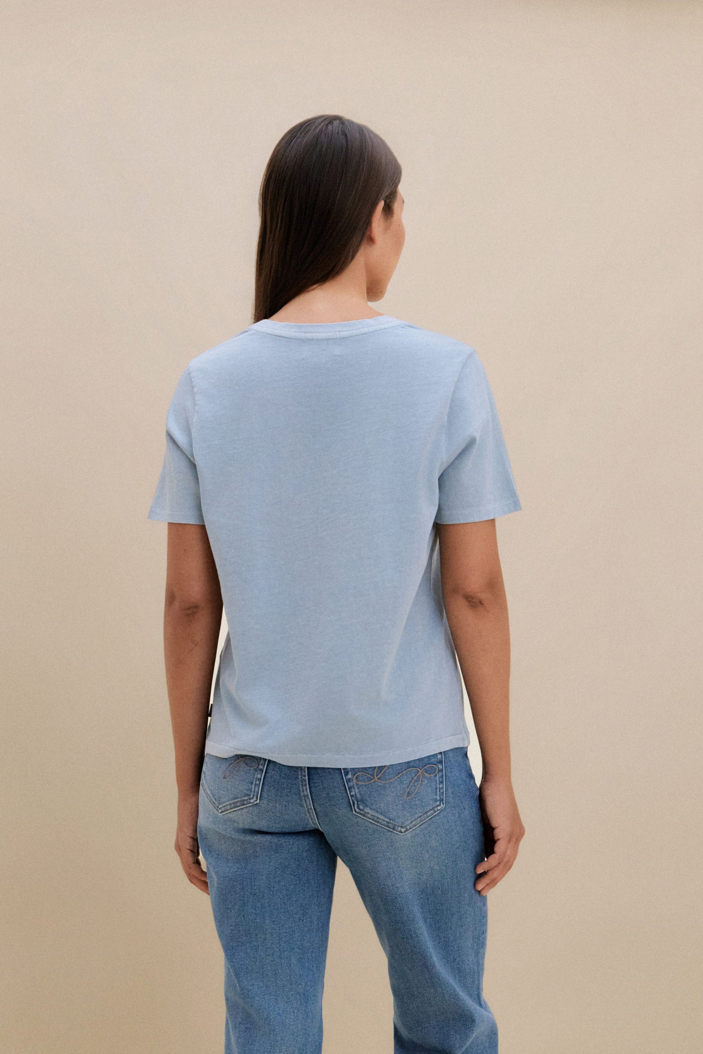 Person wearing a light blue t-shirt and jeans on a beige background