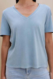 woman wearing light blue t-shirt and light colored denim with a beige wall 