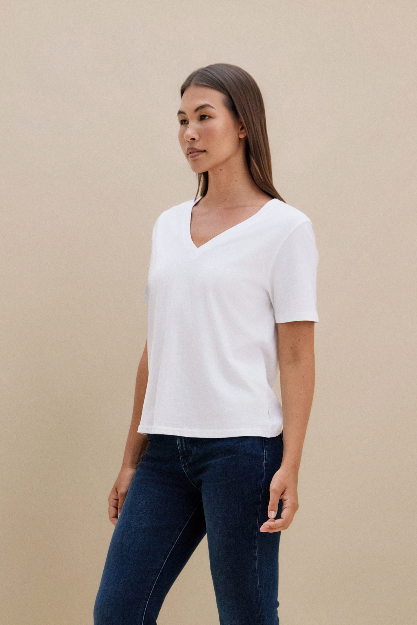 Woman wearing a plain white t-shirt and blue jeans against a beige background 