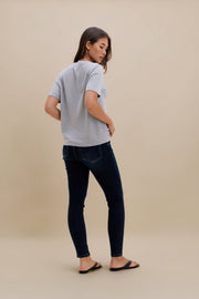 Woman wearing a light gray t-shirt and dark jeans on a beige background