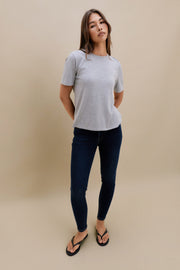 Woman wearing a gray t-shirt and dark jeans on a beige background