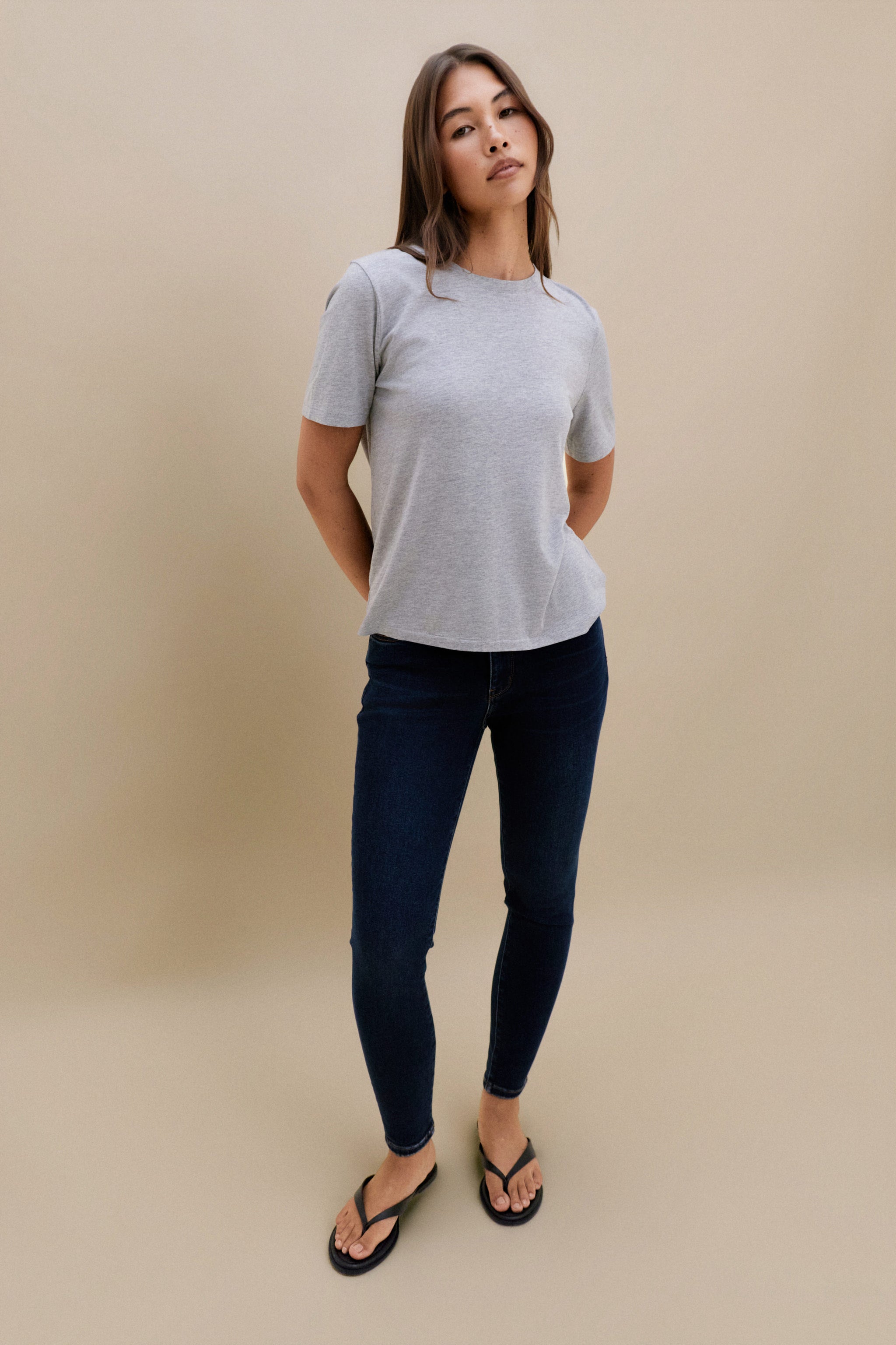 Woman wearing a gray t-shirt and dark jeans on a beige background