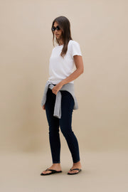 Woman wearing a white t-shirt, black pants, and sunglasses on a beige background