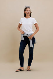 Woman wearing a white t-shirt and dark jeans against a beige background | model-size: 4