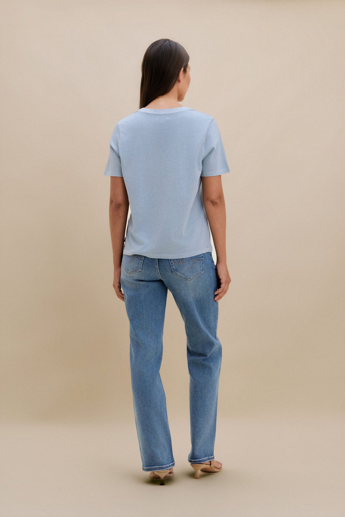 Person wearing a light blue t-shirt and jeans against a beige background