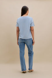 Person wearing a light blue t-shirt and jeans against a beige background