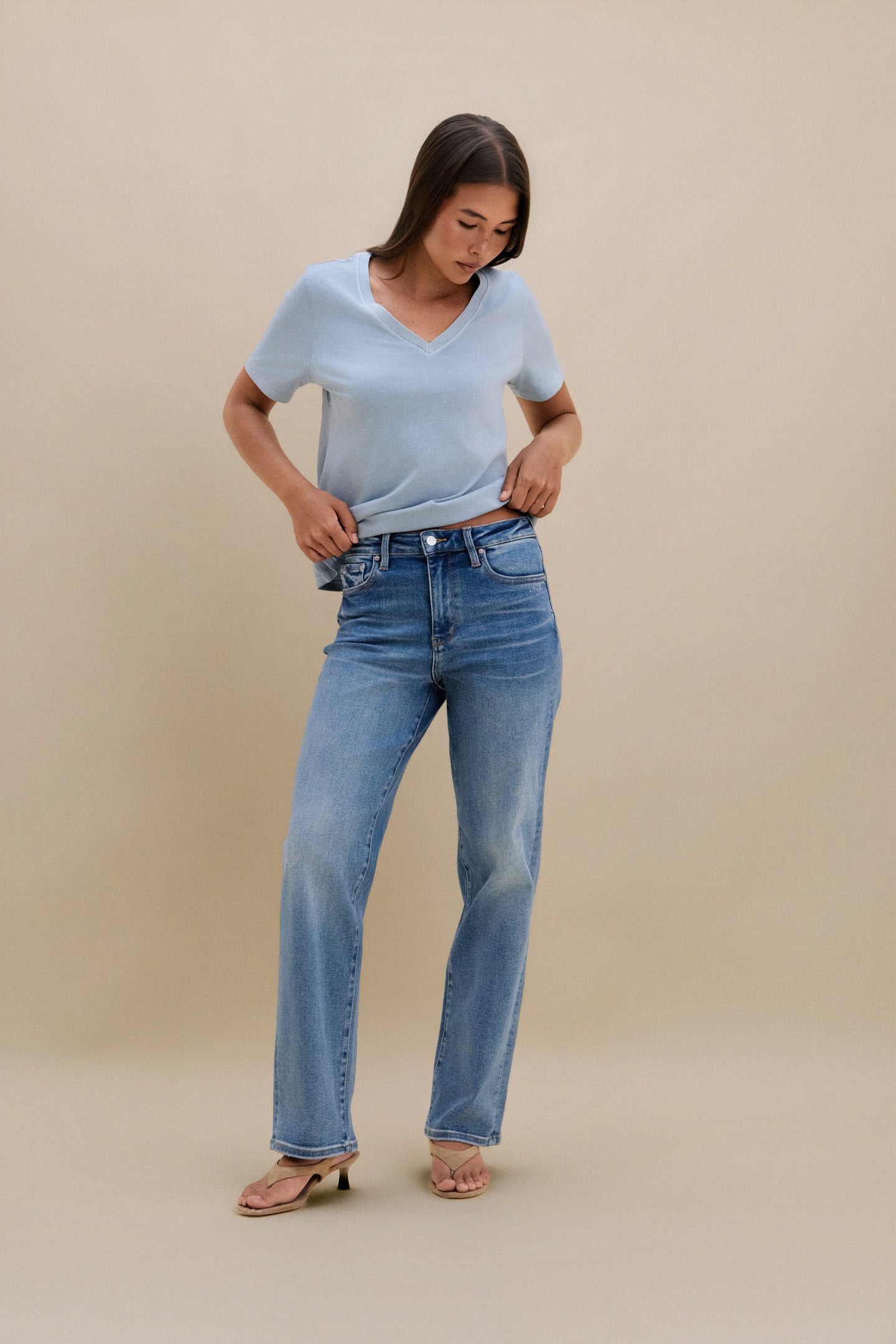 Woman wearing a light blue t-shirt and blue jeans against a beige background