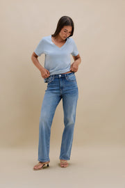 Woman wearing a light blue t-shirt and blue jeans against a beige background