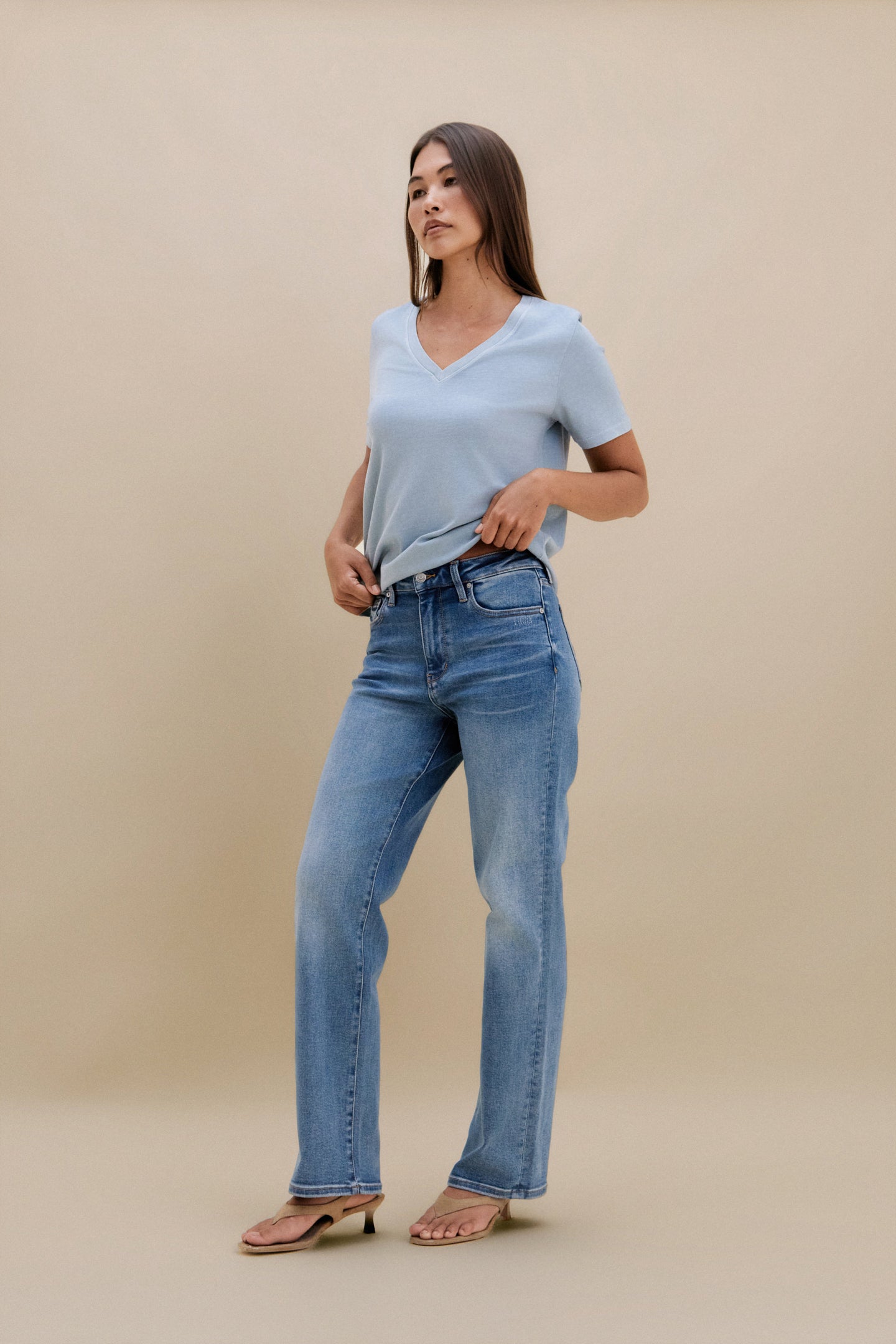 Woman wearing a light blue t-shirt and jeans against a beige background