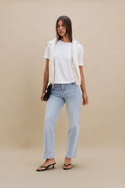 Woman wearing a white top and light blue jeans against a beige background | model-size: 4