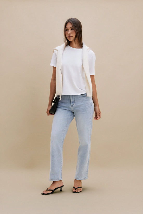 Woman wearing a white top and light blue jeans against a beige background | model-size: 4