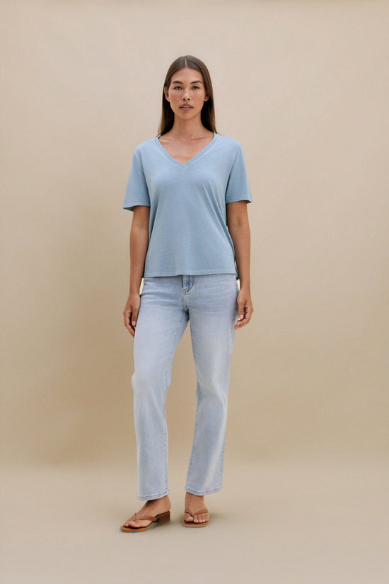 Woman wearing a light blue t-shirt and jeans against a beige background