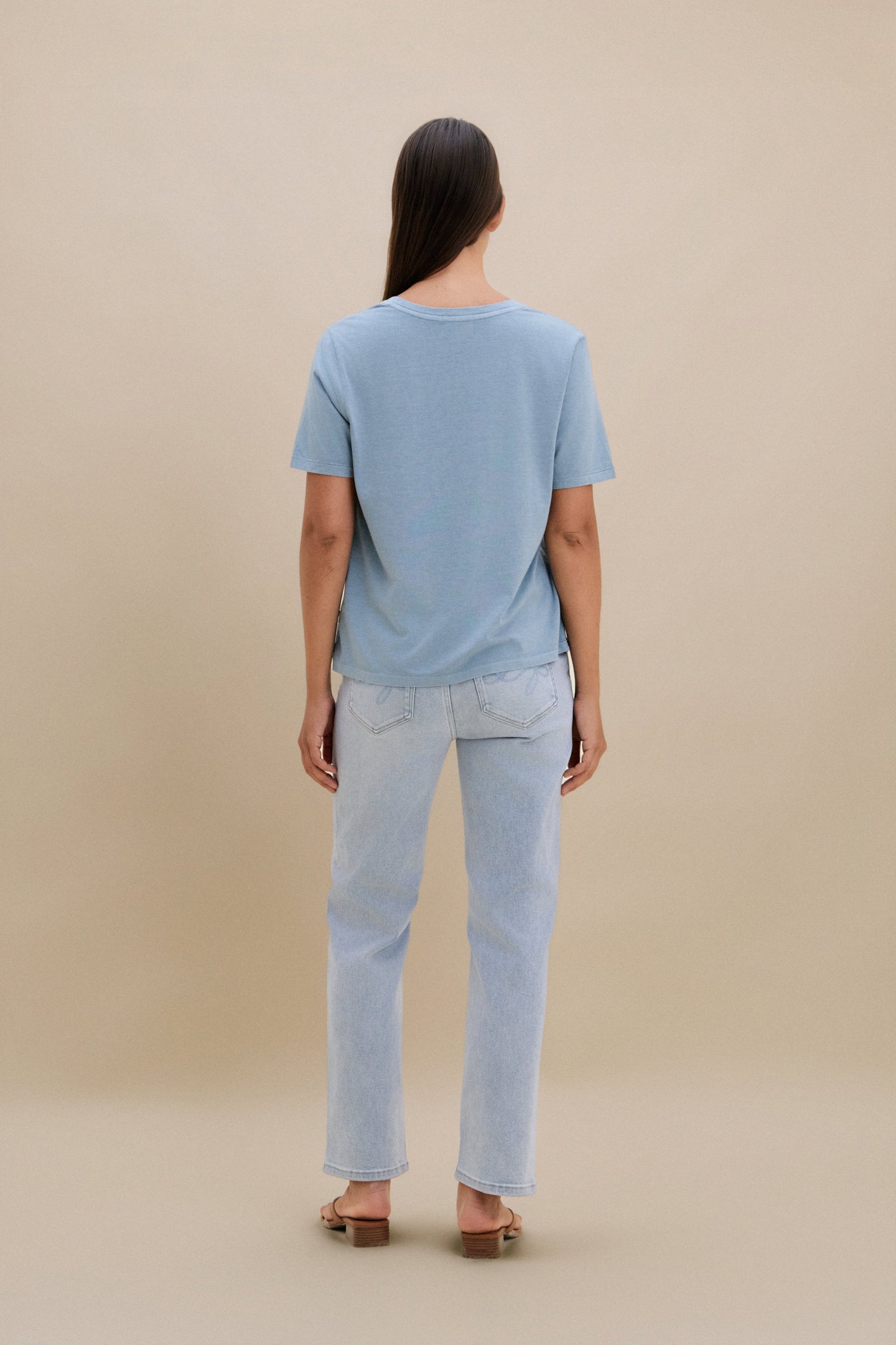 Person wearing a light blue t-shirt and jeans on a beige background