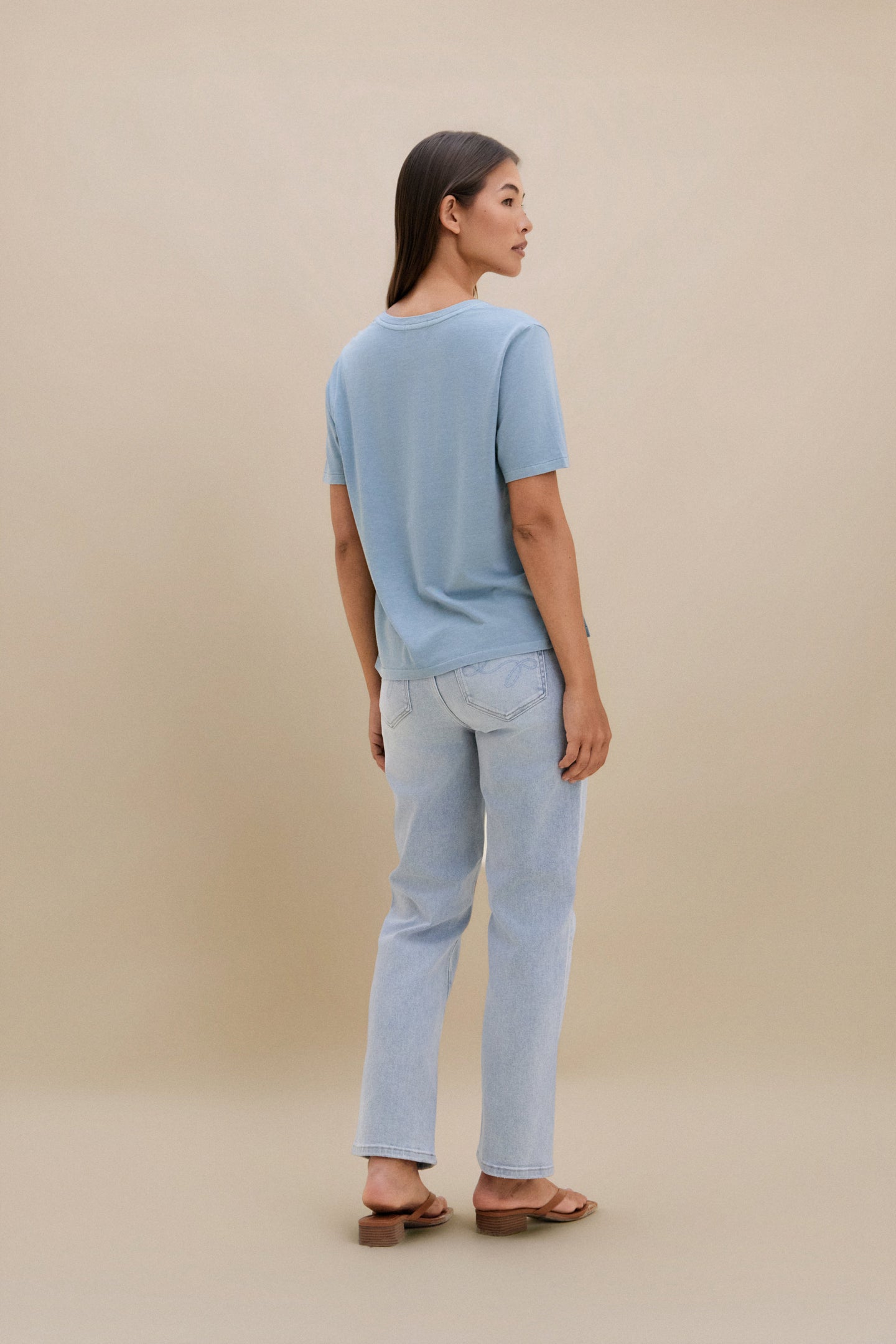 Woman wearing a light blue t-shirt and jeans against a beige background