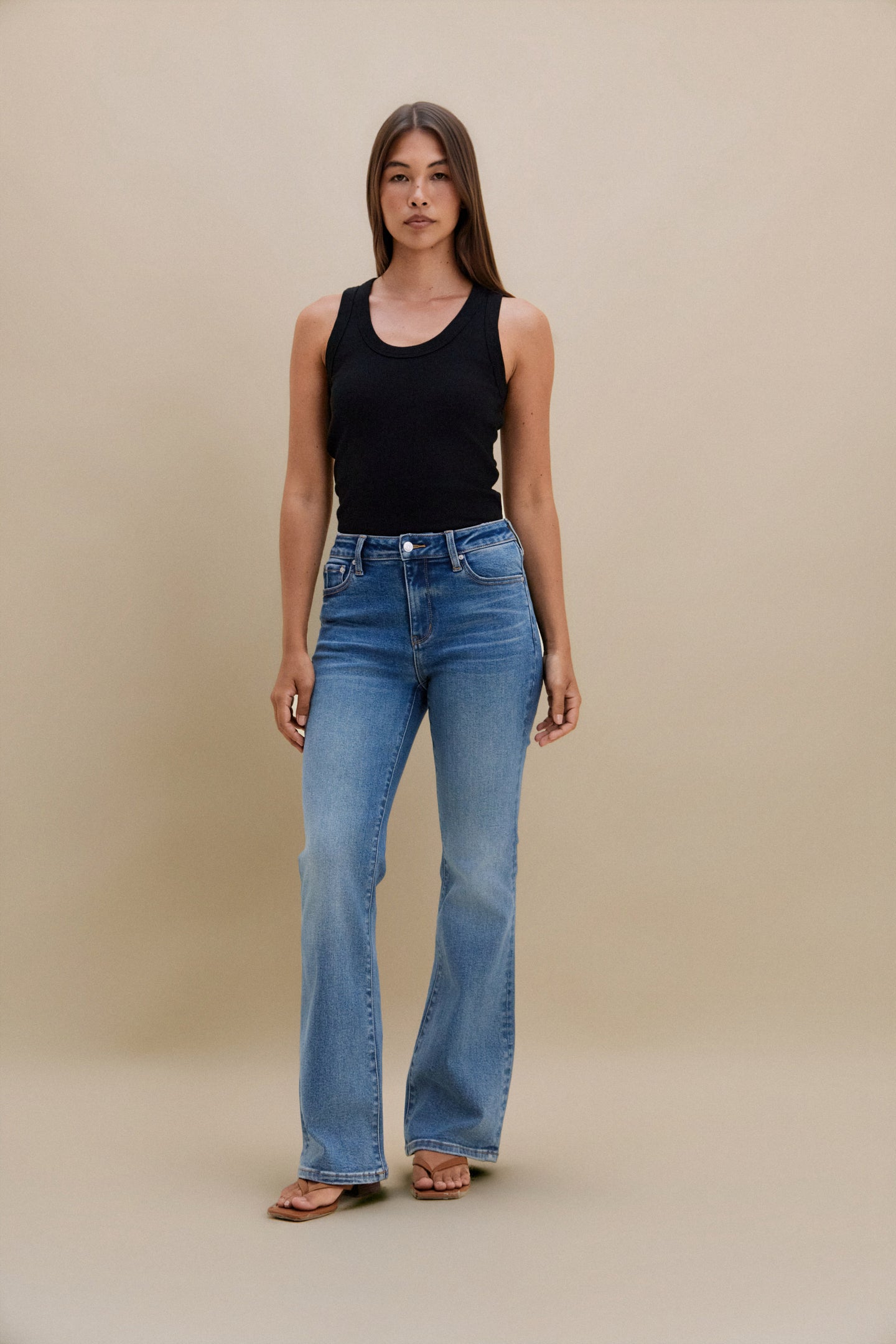 Woman wearing a black tank top and blue jeans against a beige background | model-size: 4