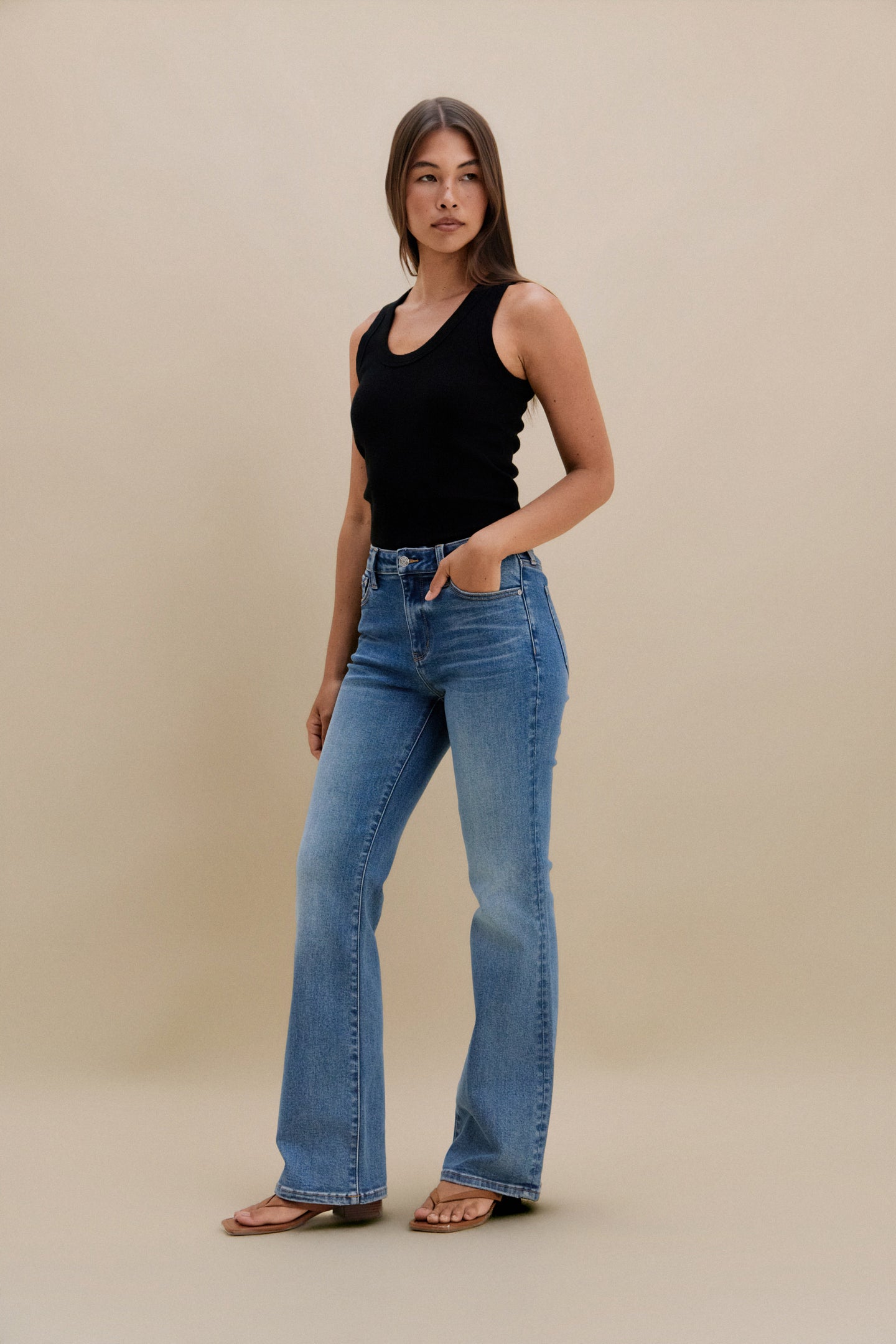 Woman wearing a black tank top and blue jeans against a beige background