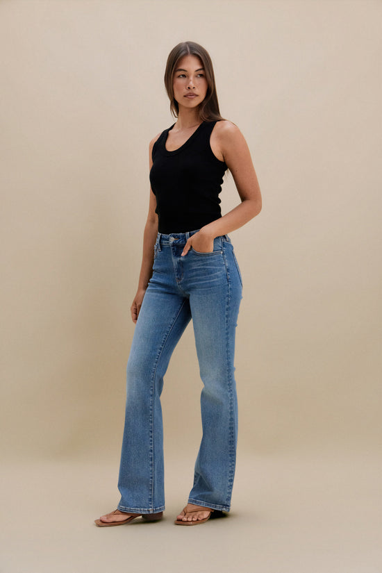 Woman wearing a black tank top and blue jeans against a beige background