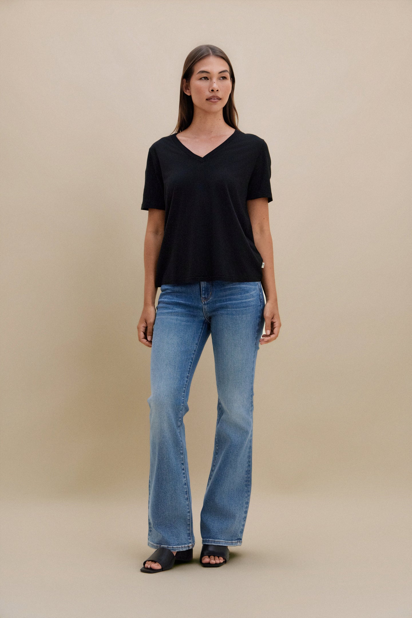 Woman wearing a black V-neck shirt and blue jeans against a beige background