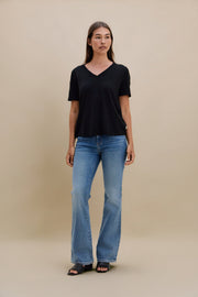 Woman wearing a black V-neck shirt and blue jeans against a beige background