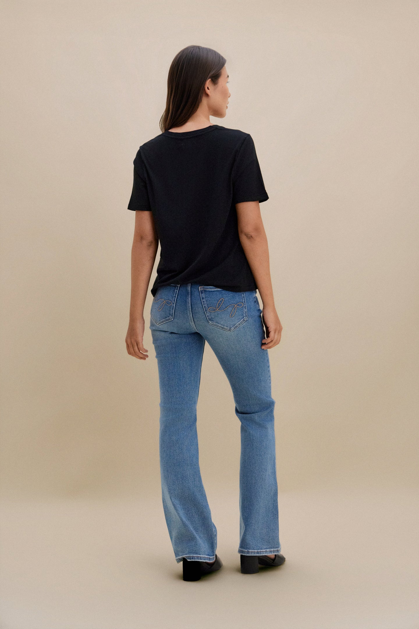 Person wearing a black t-shirt and blue jeans on a beige background