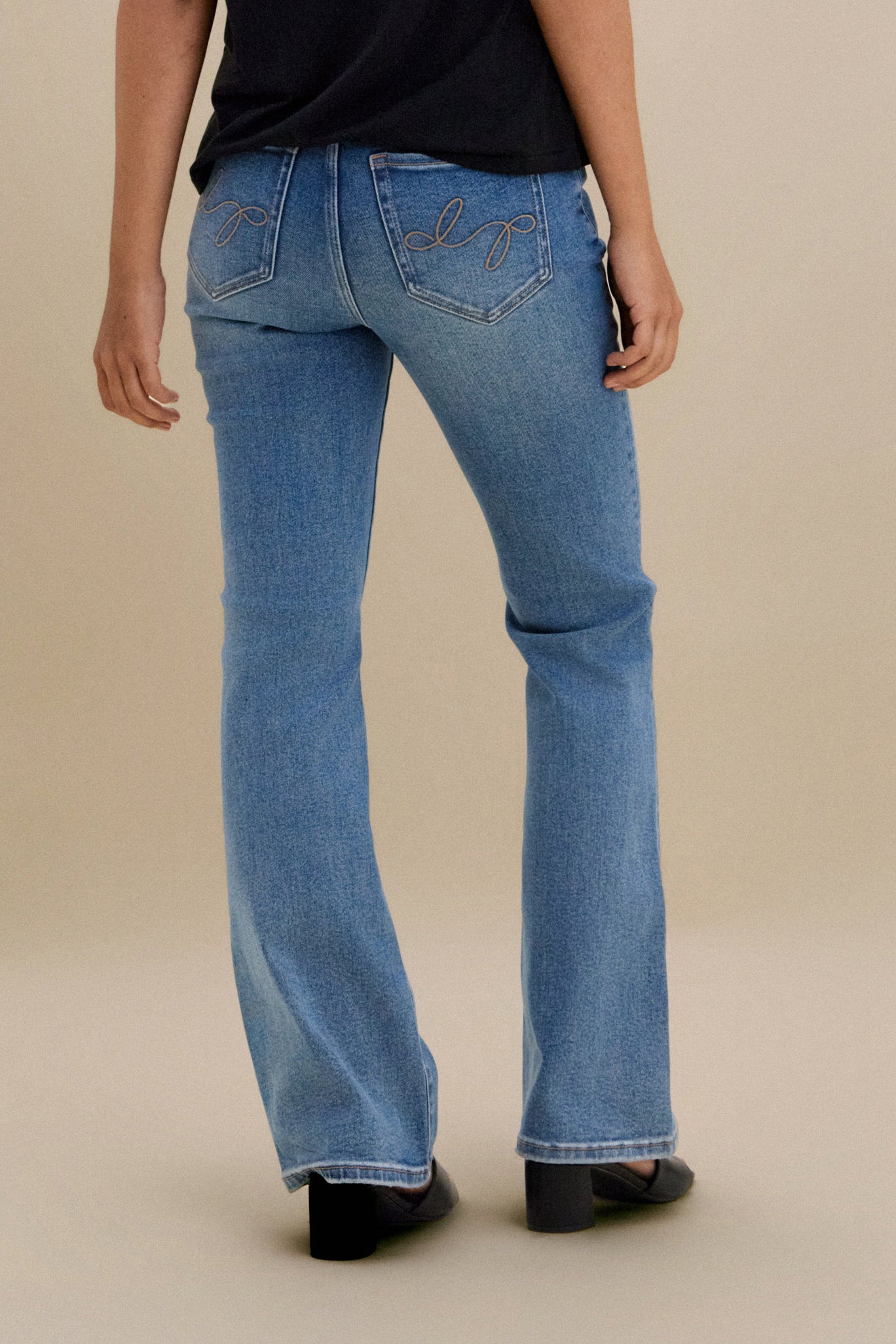 Bottom close up, backside, of bootcut jeans against a beige background