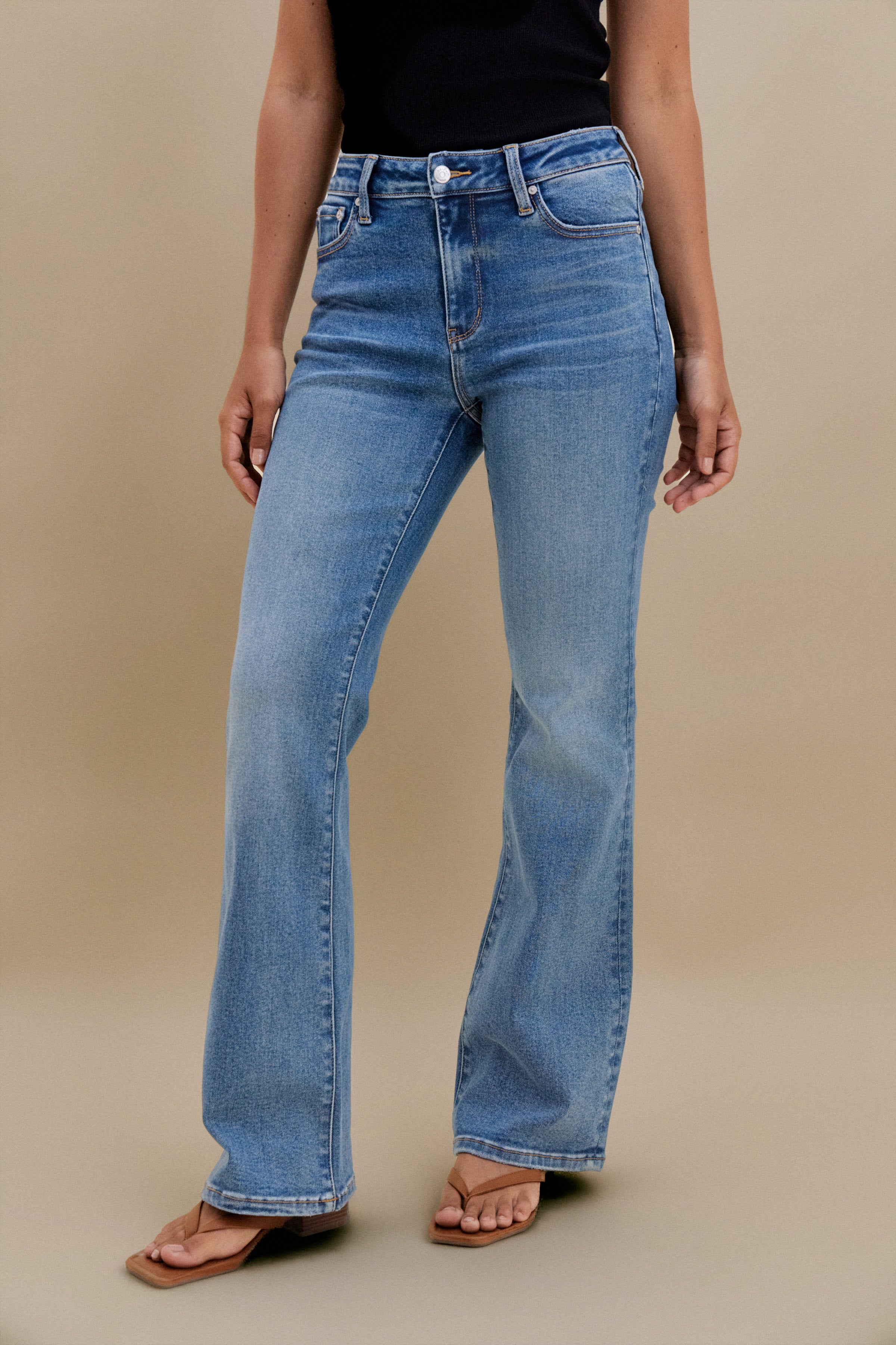 Bottom close up of bootcut jeans against a beige background