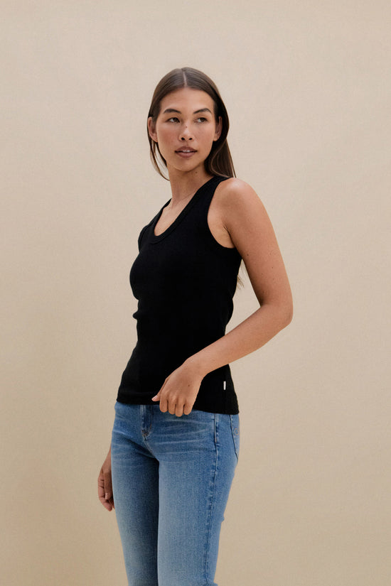 Woman wearing a black tank top and blue jeans against a beige background | model-size: 4