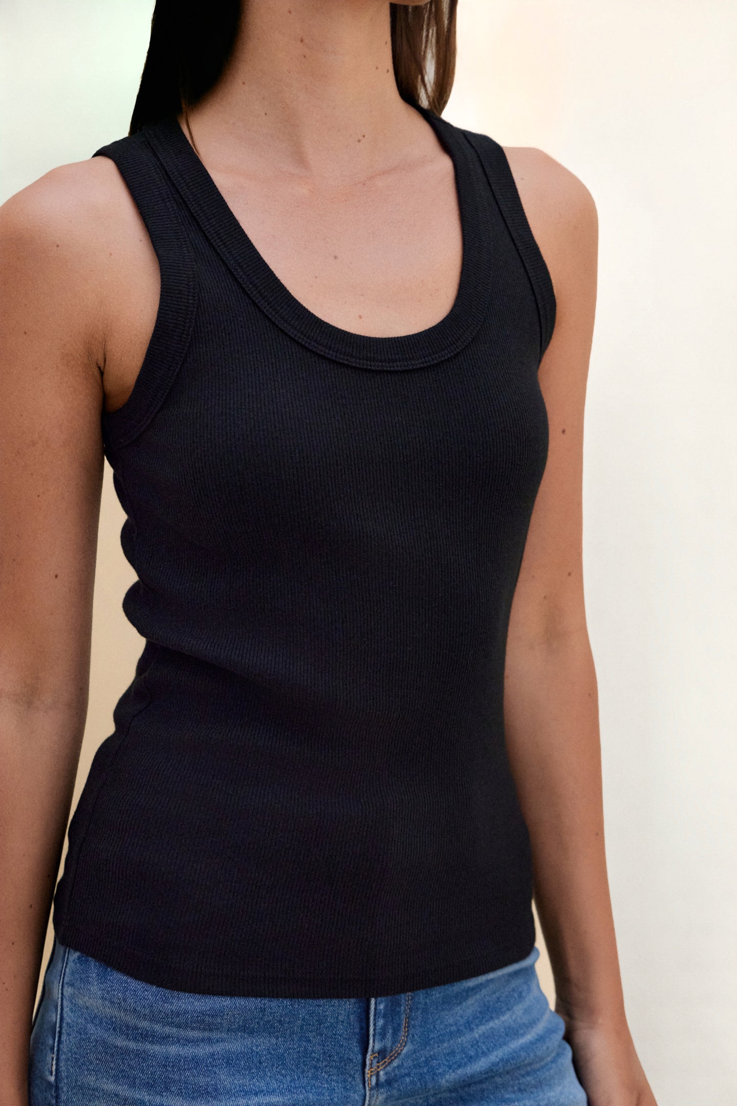 Person wearing a black tank top and blue jeans against a neutral background