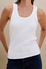Person wearing a white tank top against a beige background