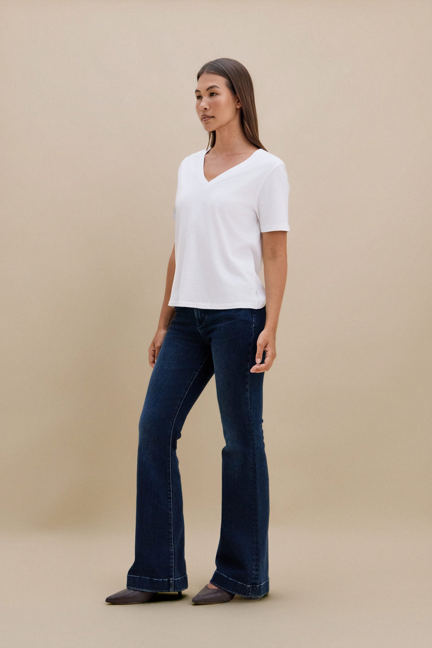 Woman wearing a white shirt and dark blue jeans against a beige background