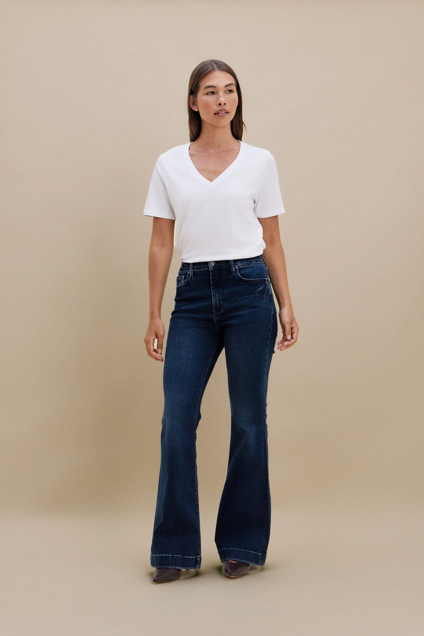 Woman wearing a white top and blue jeans against a beige background