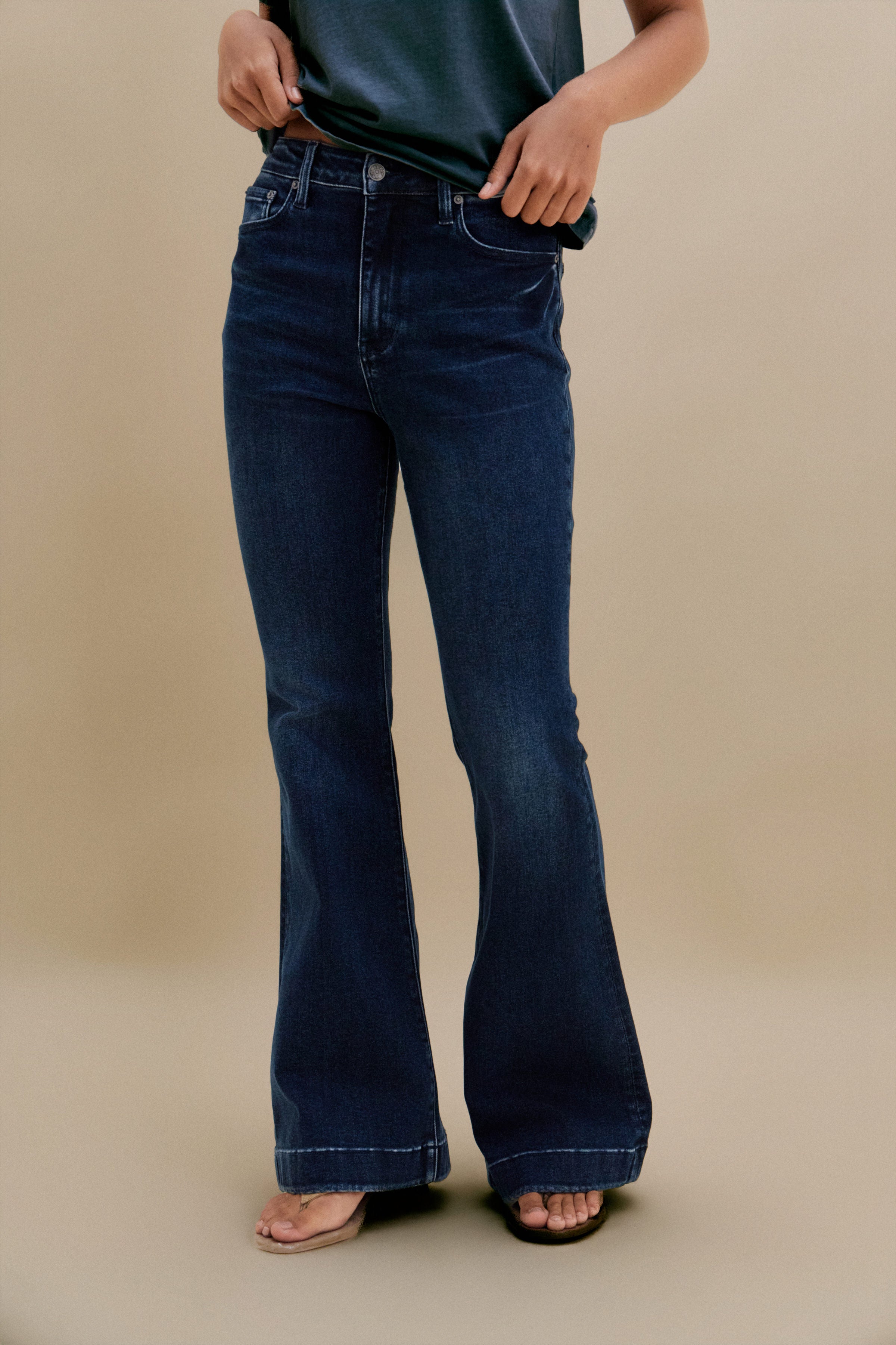 Bottom close up of dark flare jeans against a beige background