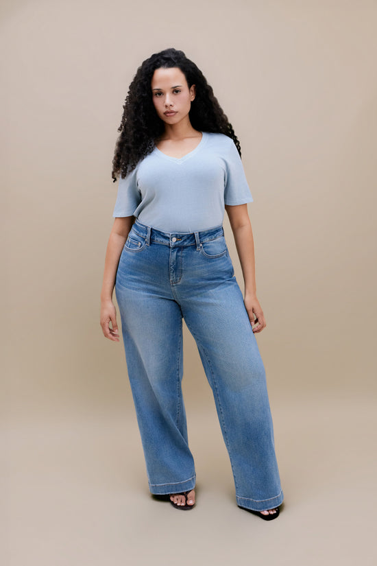 Woman wearing a blue t-shirt and wide leg jeans with a beige background | model-size: 16