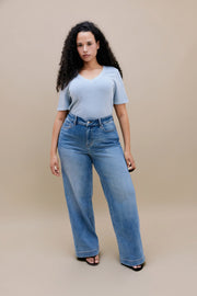 Woman wearing a blue t-shirt and wide leg jeans with a beige background | model-size: 16