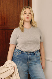 Woman wearing a gray t-shirt and blue jeans standing against a wooden door | model-size: 16