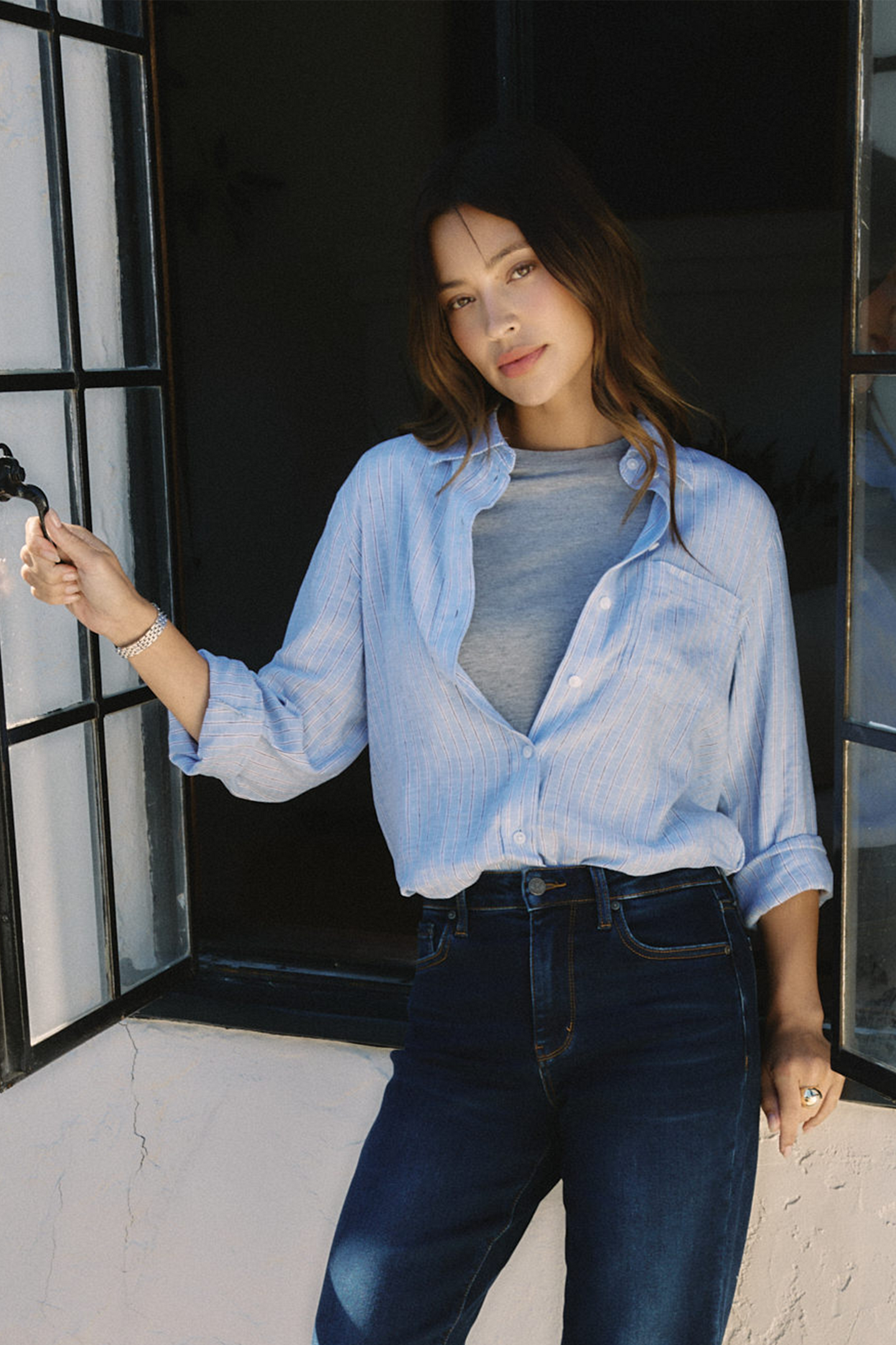 Woman wearing a light blue shirt and dark jeans standing outdoors | model-size: 4