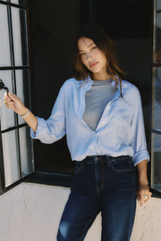Woman wearing a light blue shirt and dark jeans standing outdoors | model-size: 4