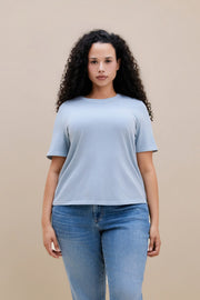 Woman wearing a blue crew neck tee and jeans with a beige background | model-size: 16