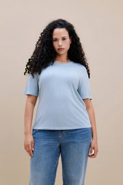 Woman wearing a light blue t-shirt and jean against a beige background 