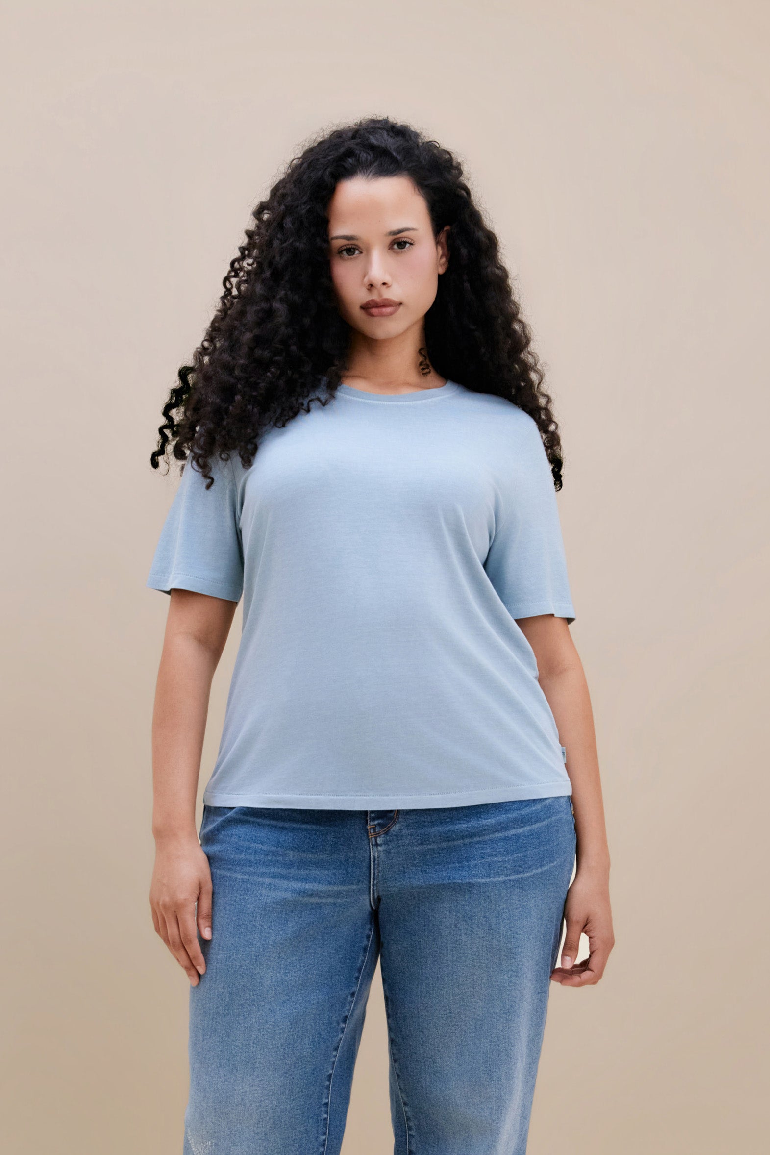 Woman wearing a light blue t-shirt and jean against a beige background 