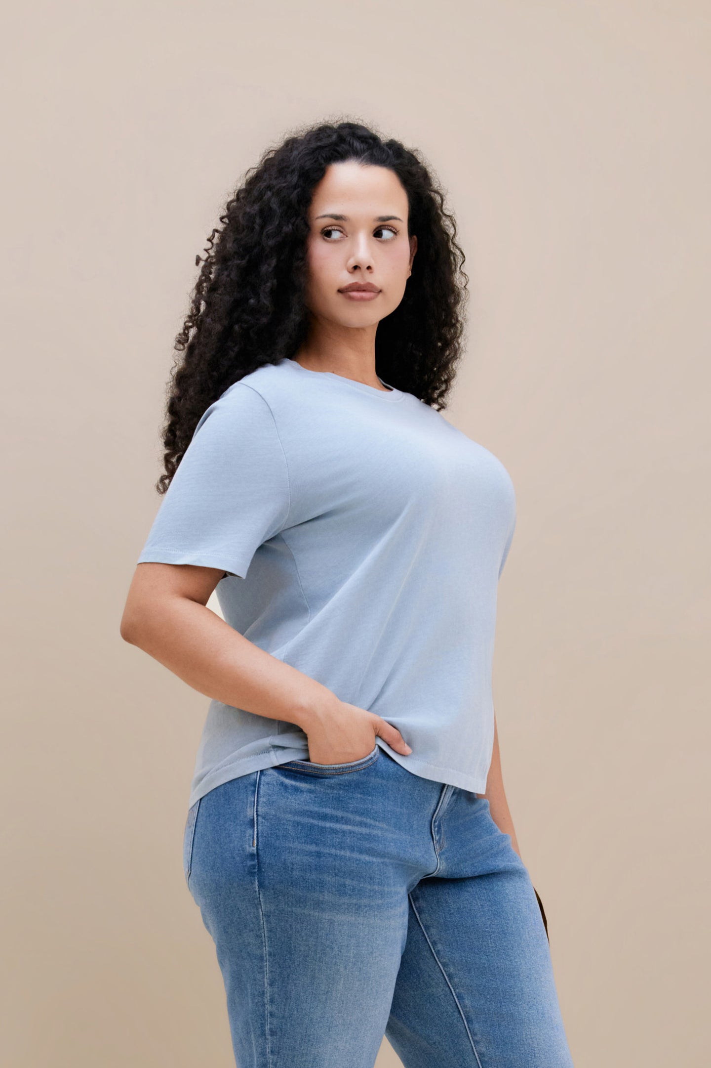 Woman wearing a blue crew neck tee and jeans with a beige background 