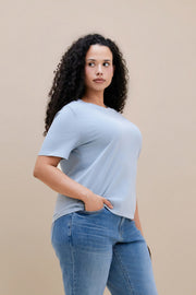 Woman wearing a blue crew neck tee and jeans with a beige background 