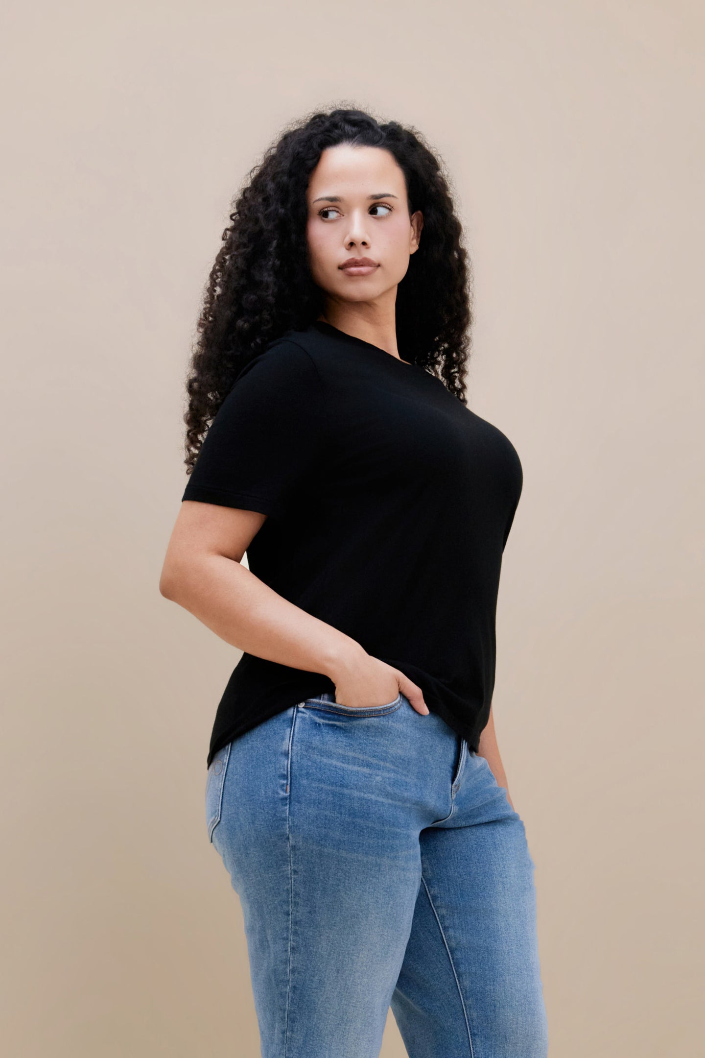Woman wearing a black t-shirt and blue jeans against a beige background 