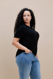 Woman wearing a black t-shirt and blue jeans against a beige background 