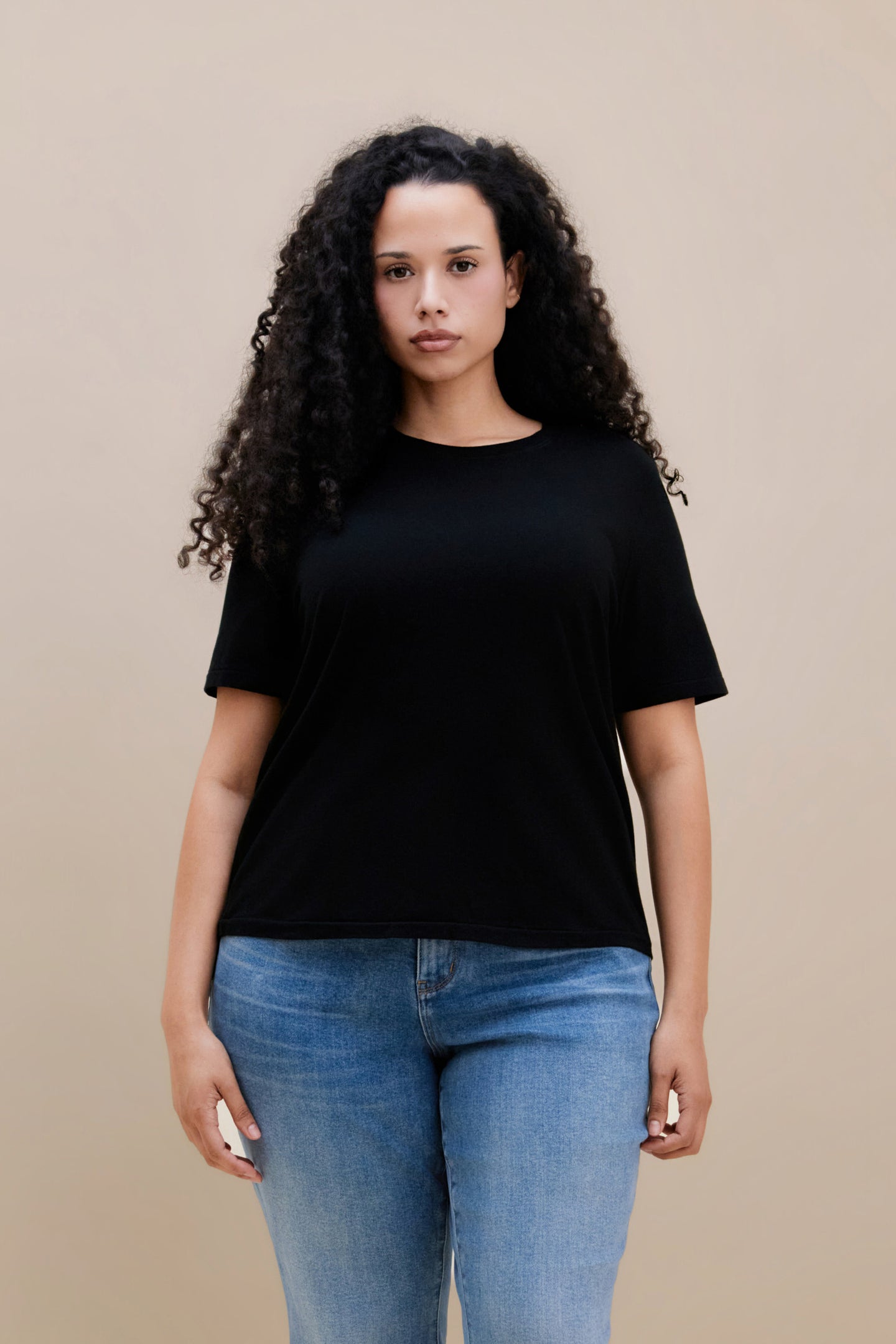 Woman wearing a black t-shirt and blue jeans against a beige background | model-size: 16