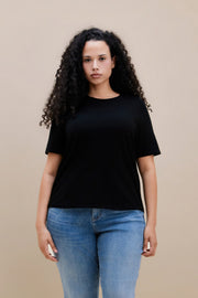 Woman wearing a black t-shirt and blue jeans against a beige background | model-size: 16