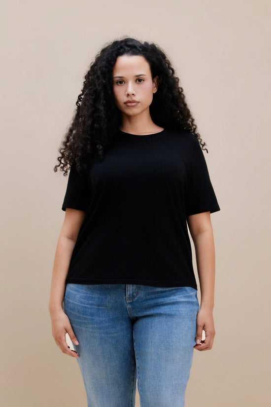 Woman wearing a black t-shirt and blue jeans against a beige background | model-size: 16