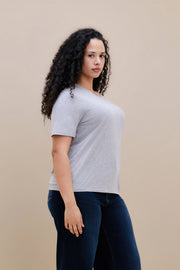 Woman wearing a light heather grey t-shirt  & dark jeans against a beige background