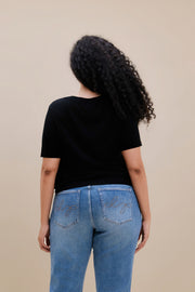 Backside of a woman wearing a black t-shirt with jeans against a beige background