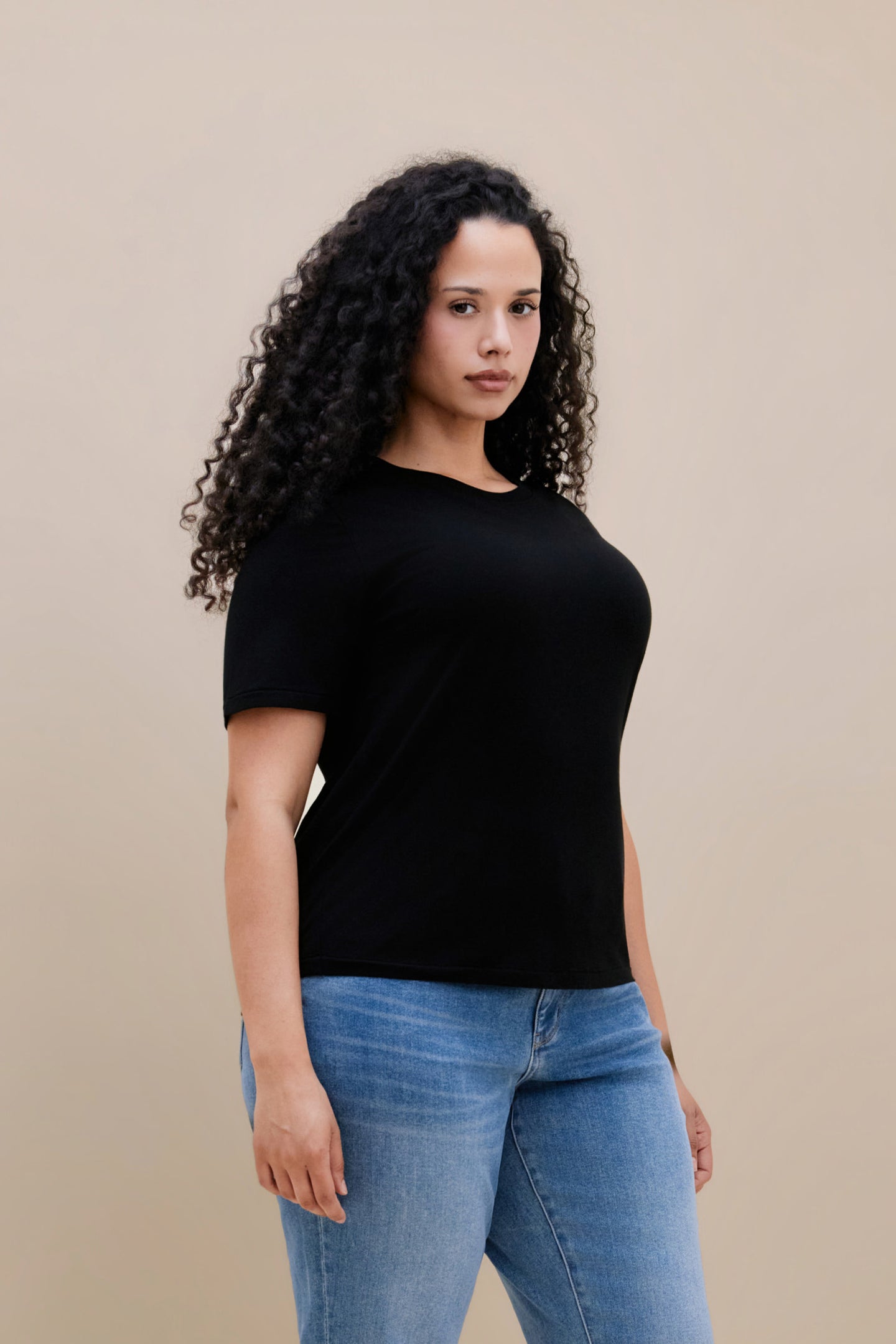 Woman wearing a black t-shirt with jeans against a beige background